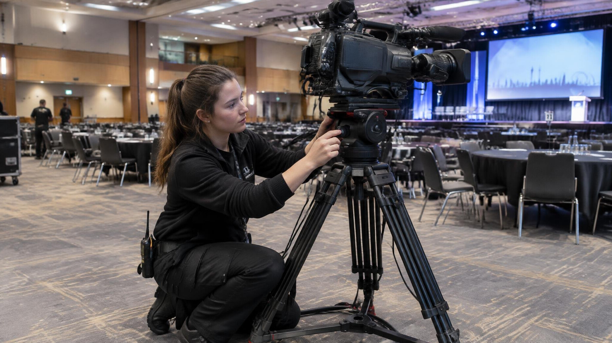 Technician setting up a video camera on a tripod at an event venue